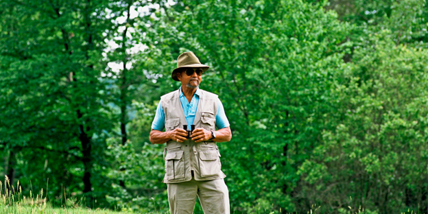 Man with binoculars with green trees in background